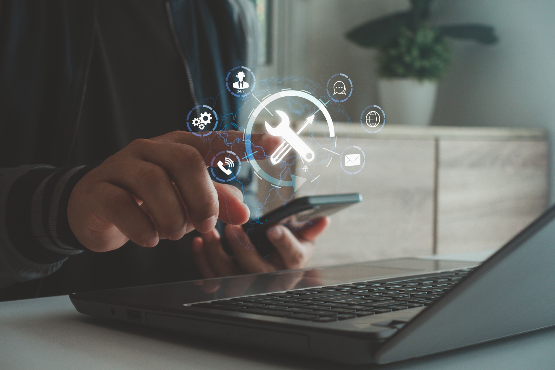 Person using smartphone and laptop with digital icons of tools, settings and gears symbolizing online technical support, system maintenance, IT service management, and digital business solutions.